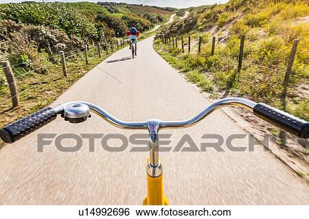 Stock Photograph - Cycling along rural road between dunes near Den Haag, personal perspective, Scheveningen, South Holland, Netherlands. Fotosearch