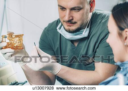 Stock Photo - Dentist explaining dental implant procedure to patient. Fotosearch