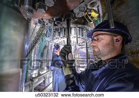 Stock Image - Engineer working in confined space under turbine during outage in nuclear power station. Fotosearch