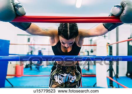 Stock Image - Exhausted female boxer leaning over boxing ring ropes. Fotosearch