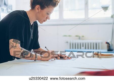 Stock Image - Fashion designer drawing and creating dressmaker's pattern. Fotosearch