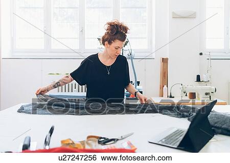 Stock Photograph - Fashion designer laying out fabric on workbench. Fotosearch