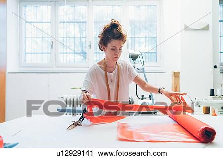 Stock Image - Fashion designer unrolling textile on workbench. Fotosearch
