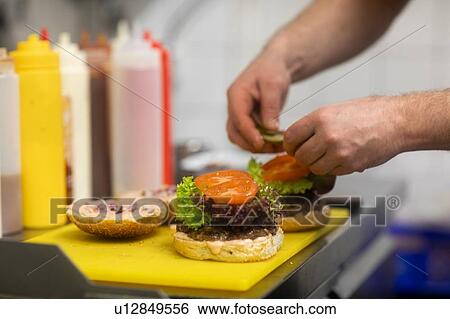 Fast food worker adding salad to hamburger in commercial kitchen, close up of hand View Large Photo Image Stock Photograph - Fast food worker adding salad to hamburger in commercial kitchen, close up of hand. Fotosearch