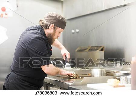Stock Image - Fast food worker frying burger in commercial kitchen. Fotosearch