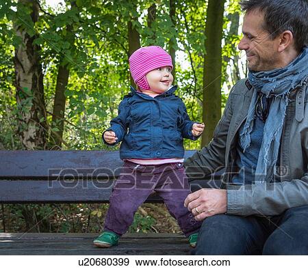 Stock Photo - Father and baby girl on park bench by forest. Fotosearch