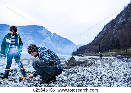 Stock Photography - Father and son starting campfire, Onno, Lombardy, Italy. Fotosearch