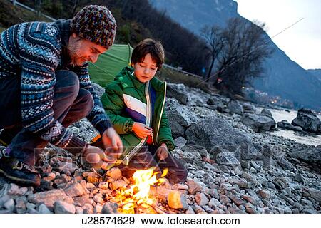 Stock Photo - Father and son toasting marshmallows over campfire, Onno, Lombardy, Italy. Fotosearch