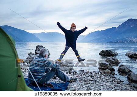 Father watching son doing star jump by lakeside, Onno, Lombardy, Italy View Large Photo Image Stock Photography - Father watching son doing star jump by lakeside, Onno, Lombardy, Italy. Fotosearch