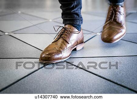 Stock Image - Feet in pair of brogues on tiled flooring. Fotosearch