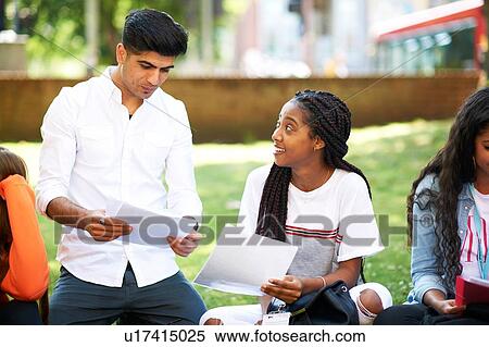 Stock Photography - Female and male higher education students discussing paperwork on college campus lawn. Fotosearch