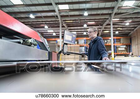 Stock Image - Female printing machine operator in cardboard box factory. Fotosearch