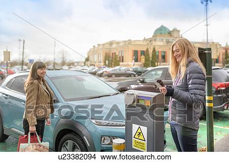 Picture - Female shoppers charging electric car at charge point, Manchester, UK. Fotosearch