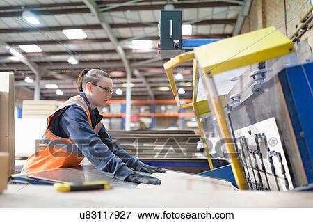 Stock Photo - Female worker operating cutting machine in cardboard box factory. Fotosearch