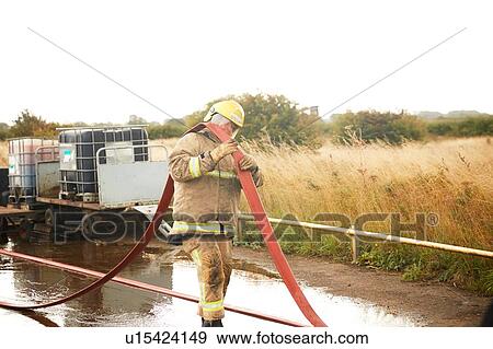 Stock Photo - Firemen training, fireman carrying fire hose over his shoulder at training facility. Fotosearch
