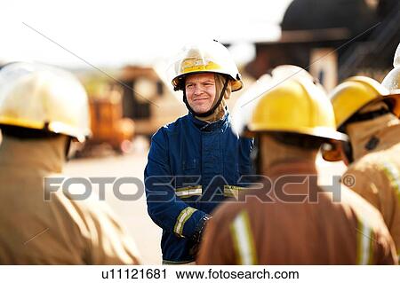 Stock Image - Firemen training, firemen listening to supervisor at training facility, over shoulder view. Fotosearch