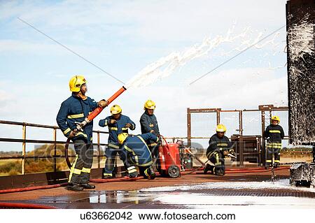 Stock Image - Firemen training, firemen spraying firefighting foam at training facility. Fotosearch