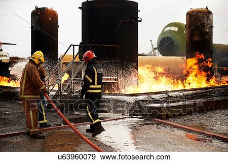 Stock Photo - Firemen training, spraying firefighting foam onto oil storage tank fire at training facility. Fotosearch