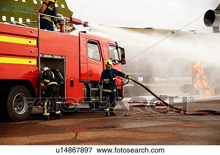 Stock Photo - Firemen training, spraying water from fire engine at mock airplane engine. Fotosearch