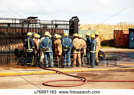 Stock Image - Firemen training, team of firemen listening to supervisor at training facility, rear view. Fotosearch