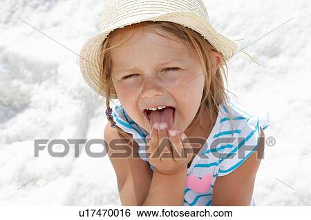 Stock Photograph - Girl in sun hat licking her fingers on beach, portrait Trapani, Sicily, Italy. Fotosearch