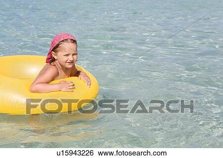 Stock Photograph - Girl playing with yellow inflatable in sea, San Vito, Sicily, Italy. Fotosearch