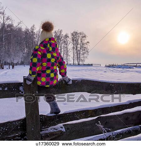 Girl sitting on fence in snow covered landscape at sunset, rear view View Large Photo Image Stock Photo - Girl sitting on fence in snow covered landscape at sunset, rear view. Fotosearch