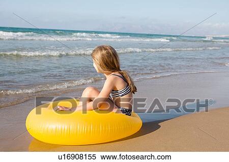 Stock Photography - Girl sitting on yellow inflatable at beach, Castellammare del Golfo, Sicily, Italy. Fotosearch