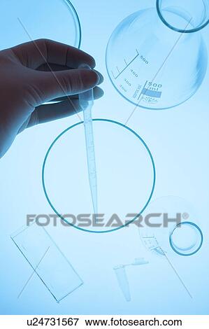 Stock Photo - Hand holding pipette over assortment of laboratory glassware.. Fotosearch