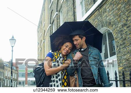 Happy couple under umbrella in street, London, UK View Large Photo Image Stock Photo - Happy couple under umbrella in street, London, UK. Fotosearch