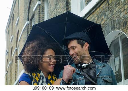 Stock Photo - Happy couple under umbrella in street, London, UK. Fotosearch