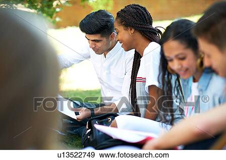 Higher education students looking at paperwork on college campus lawn, over shoulder view View Large Photo Image Stock Photo - Higher education students looking at paperwork on college campus lawn, over shoulder view. Fotosearch