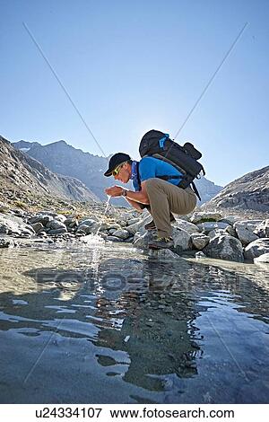 Stock Photo - Hiker drinking from pool, Mont Cervin, Matterhorn, Valais, Switzerland. Fotosearch