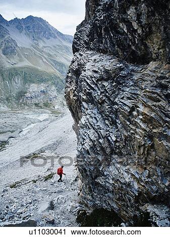 Stock Image - Hiker moving across rocky terrain, Mont Cervin, Matterhorn, Valais, Switzerland. Fotosearch