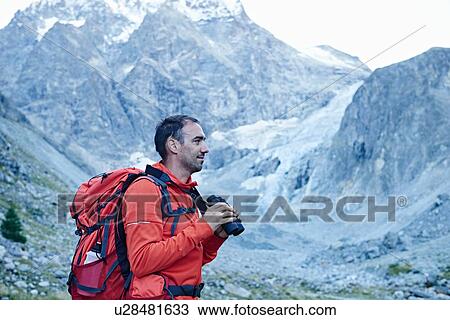 Stock Image - Hiker using binoculars, Mont Cervin, Matterhorn, Valais, Switzerland. Fotosearch