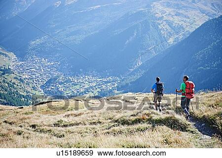 Stock Photo - Hikers on grassy cliff overlooking valley, Mont Cervin, Matterhorn, Valais, Switzerland. Fotosearch