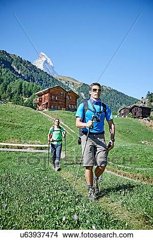 Picture - Hikers on lush green field, chalets in background, Mont Cervin, Matterhorn, Valais, Switzerland. Fotosearch