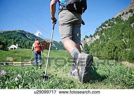 Stock Photo - Hikers on lush green field, chalets in background, Mont Cervin, Matterhorn, Valais, Switzerland. Fotosearch
