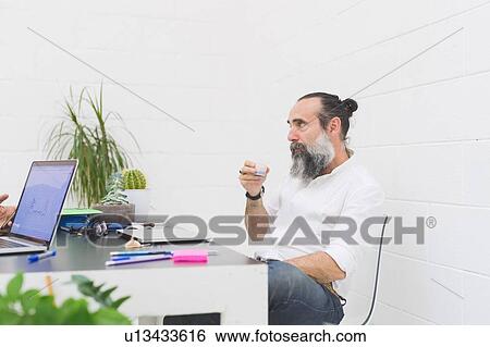 Stock Photograph - Hipster businessman drinking water at office desk. Fotosearch