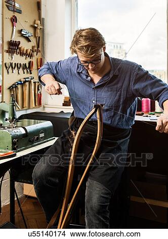 Picture - Leatherworker stitching leather handbag straps in workshop. Fotosearch