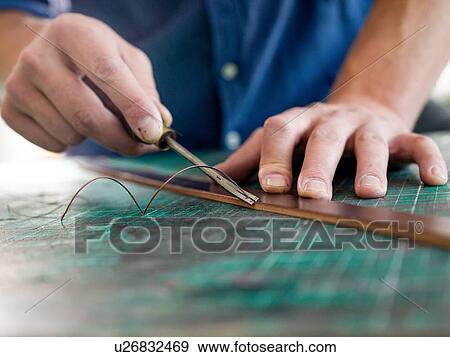 Stock Photo - Leatherworker trimming leather for handbag strap in workshop, close up of hands. Fotosearch