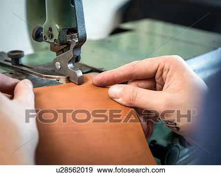 Stock Photo - Leatherworker using machining leather handbag edge in workshop, close up of hands. Fotosearch
