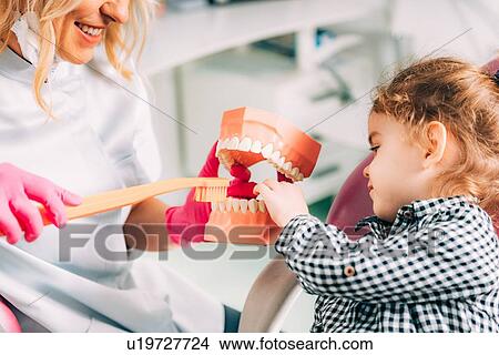 Picture - Little girl at dental clinic, learning how to brush teeth correctly.. Fotosearch