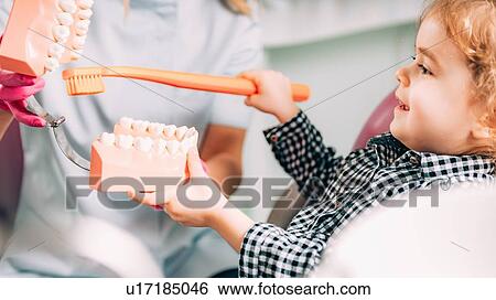 Stock Photograph - Little girl at dental clinic, learning how to brush teeth correctly.. Fotosearch