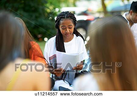 Stock Photo - Male and female higher education student looking at paperwork on college campus lawn, over shoulder view. Fotosearch