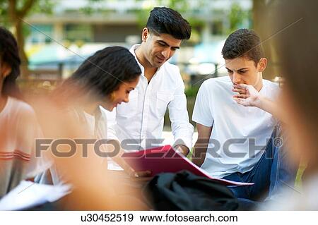 Stock Photo - Male and female higher education students looking at paperwork on college campus lawn, over shoulder view. Fotosearch