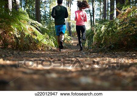 Stock Photo - Male and female runners running in forest, rear view. Fotosearch
