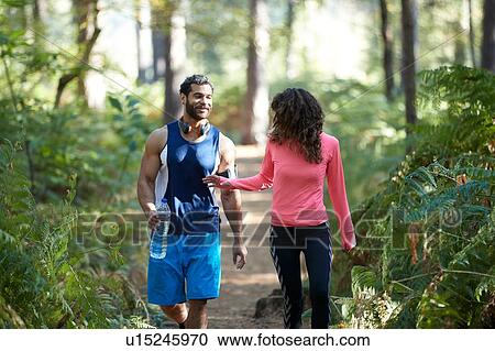 Stock Image - Male and female runners sharing bottled water in forest. Fotosearch