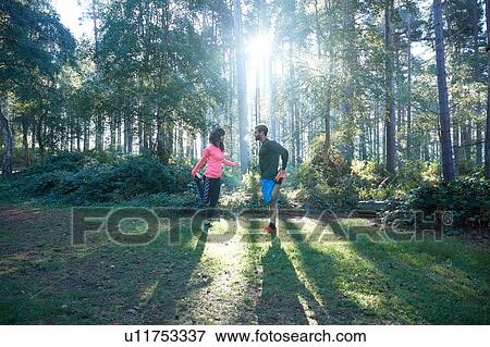 Male and female runners stretching legs and warming up in sunlit forest View Large Photo Image Stock Photo - Male and female runners stretching legs and warming up in sunlit forest. Fotosearch