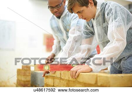 Stock Image - Male higher education students building brick wall in college workshop. Fotosearch